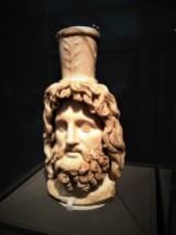 Head of Serapis. Roman, c. 200 CE; found in Walbrook, City of London. Worship of the god Serapis, the consort of Isis, spread from Egypt to the far reaches of the Roman Empire. This marble head was discovered in the Temple of Mithras in London in 1954. It may have been dedicated there when the Roman emperor Septimius Severus (ruled 193-211 CE) visited the city in 208 CE. The North African-born ruler particularly revered Serapis and styled his own portraiture on the deity's appearance.